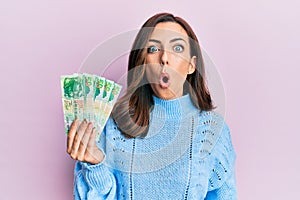 Young brunette woman holding hong kong 50 dollars banknotes scared and amazed with open mouth for surprise, disbelief face