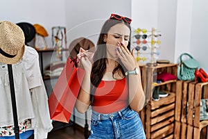 Young brunette woman holding shopping bags at retail shop bored yawning tired covering mouth with hand