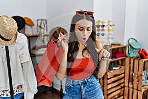 Young brunette woman holding shopping bags at retail shop pointing down with fingers showing advertisement, surprised face and