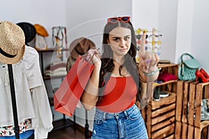 Young brunette woman holding shopping bags at retail shop pointing with finger up and angry expression, showing no gesture