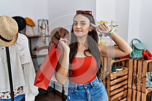 Young brunette woman holding shopping bags at retail shop smiling pointing to head with one finger, great idea or thought, good