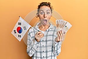 Young brunette woman holding south korean won banknotes afraid and shocked with surprise and amazed expression, fear and excited