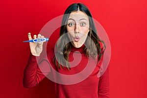 Young brunette woman holding thermometer scared and amazed with open mouth for surprise, disbelief face