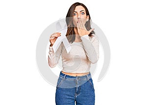 Young brunette woman holding white ribbon covering mouth with hand, shocked and afraid for mistake