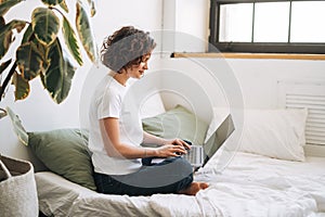 Young brunette woman in home clothes working on laptop on bed at home