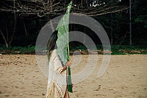 Young brunette woman with a large leaf exotic palm tree