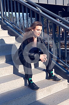 Young brunette woman in leather jacket sitting outdoors on a stair step