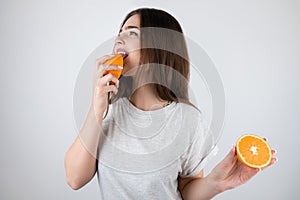 Young brunette woman licking one half of orange in tempting manner standing on isolated white background dietology and nutrition