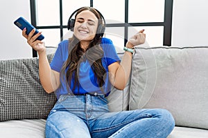 Young brunette woman listening to music from smartphone using headphones screaming proud, celebrating victory and success very