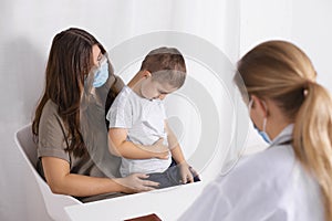 Young brunette woman with little boy having consultation at pediatrician office. Child has abdominal pain. Doctor, child