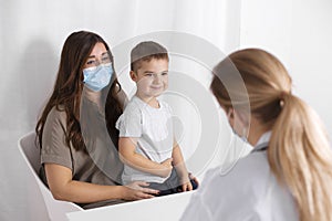 Young brunette woman with little boy having consultation at pediatrician office. Doctor, child and mother wearing