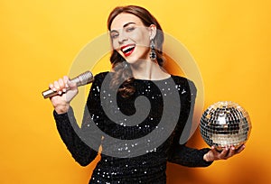 Young brunette woman with long curly hair dressed in evening dress holding a microphone and disco ball