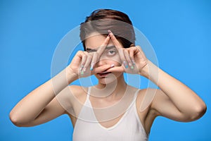 Young brunette woman looking through triangle finger frame