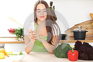 Young brunette woman is looking a new recipe for cooking at the kitchen. Housewife holding wooden spoon and table