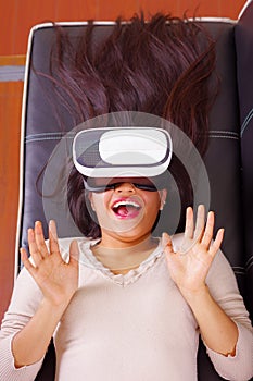 Young brunette woman lying down wearing virtual reality goggles experiencing future technology, interacting and smiling