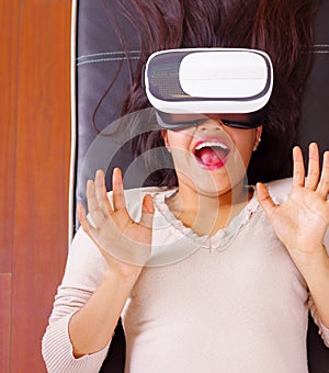 Young brunette woman lying down wearing virtual reality goggles experiencing future technology, interacting and smiling