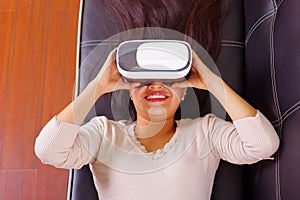 Young brunette woman lying down wearing virtual reality goggles experiencing future technology, interacting and smiling