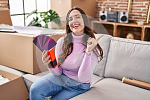 Young brunette woman moving to a new home choosing wall painting smiling happy pointing with hand and finger to the side