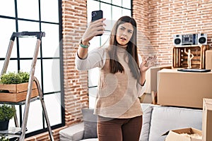 Young brunette woman moving to a new home doing video call clueless and confused expression