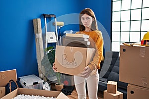 Young brunette woman moving to a new home holding box skeptic and nervous, frowning upset because of problem