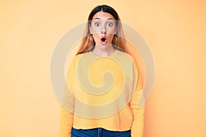 Young brunette woman over yellow background scared and amazed with open mouth for surprise, disbelief face