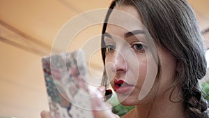 Young brunette woman paints her lips with red lipstick close up