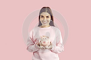 Young brunette woman with piggy bank on pink background