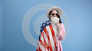 Young brunette woman in pink shirt poses on blue background in studio with american flag and hundred dollar cash