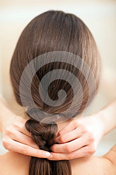Young brunette woman plaiting her hair