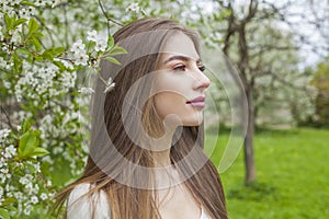 Young brunette woman portrait. Beautiful female model with long hair and make-up in spring garden outdoor