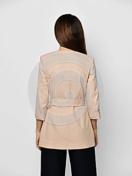 Young brunette woman is posing backwards in stylish beige formal suit jacket with cloth belt