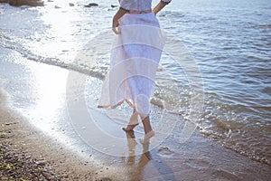 Young brunette woman posing on the morning summer beach in beautiful white dress