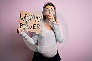 Young brunette woman pregnant expecting baby holding banner asking for women power serious face thinking about question, very