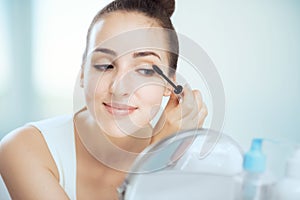 A young brunette woman putting on mascara