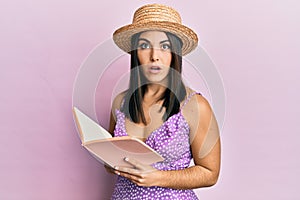 Young brunette woman reading book afraid and shocked with surprise and amazed expression, fear and excited face