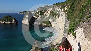 Young brunette woman in red dress descends to a tropical beach on the stairs cut down in a rock at the Diamond Beach in