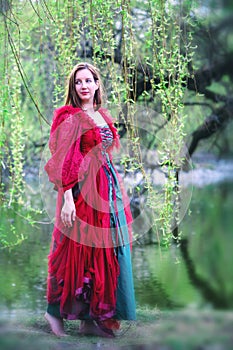 Young  brunette woman in red gown walking barefoot in nature