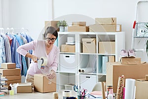 Young brunette woman sealing box with online order with cellotape