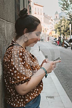 Young brunette woman searching something in her phone in the street sidewalk