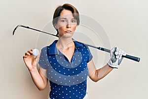 Young brunette woman with short hair holding ball and golf club depressed and worry for distress, crying angry and afraid