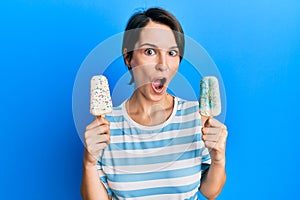 Young brunette woman with short hair holding two ice cream afraid and shocked with surprise and amazed expression, fear and