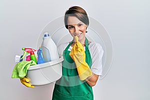 Young brunette woman with short hair wearing apron holding cleaning products beckoning come here gesture with hand inviting