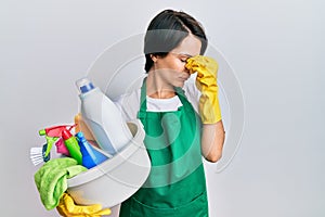 Young brunette woman with short hair wearing apron holding cleaning products tired rubbing nose and eyes feeling fatigue and