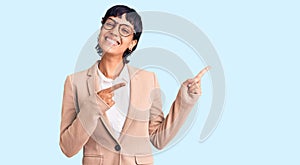 Young brunette woman with short hair wearing business jacket and glasses smiling and looking at the camera pointing with two hands