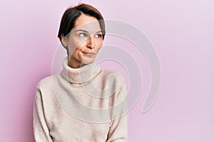 Young brunette woman with short hair wearing casual winter sweater smiling looking to the side and staring away thinking