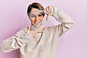 Young brunette woman with short hair wearing casual winter sweater smiling making frame with hands and fingers with happy face