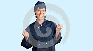 Young brunette woman with short hair wearing professional cook uniform excited for success with arms raised and eyes closed
