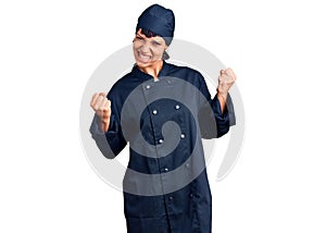 Young brunette woman with short hair wearing professional cook uniform very happy and excited doing winner gesture with arms