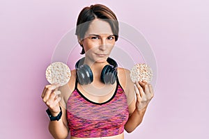 Young brunette woman with short hair wearing sportswear holding rice cakes skeptic and nervous, frowning upset because of problem