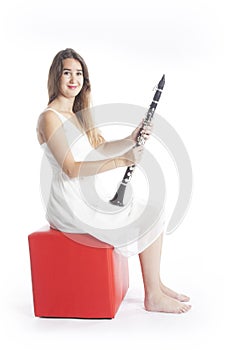 Young brunette woman sits on red stool in studio and holds clarinet